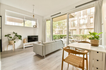 Bright and spacious living room featuring a comfortable sofa, a television, and lush greenery outside the large windows, creating a serene atmosphere.
