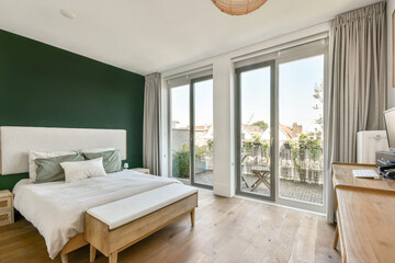 A bright and airy bedroom featuring a minimalist design with large windows, natural wood flooring, and green accent walls, creating a serene atmosphere.
