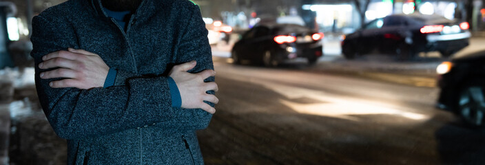 Young Man Shivering at a Bus Stop While Waiting for Public Transport in Cold Weather.