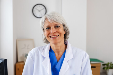 Portrait of middle aged healthcare worker standing at doctor's office. Head shot of senior female...