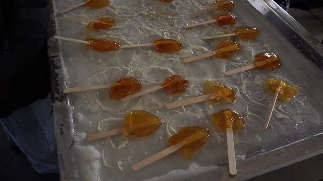 A person taking maple taffy sticks to give them to customers. All of it is on a frozen metal tray with ice.