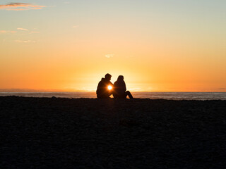 Silhouette of a young couple sitting watching enjoying the sunset at Gillespies Beach West Coast South Island New Zealand