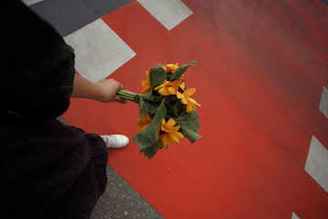 Young woman holds a bouquet of sunflowers in her hand on the  bright red pedestrian crossing background.