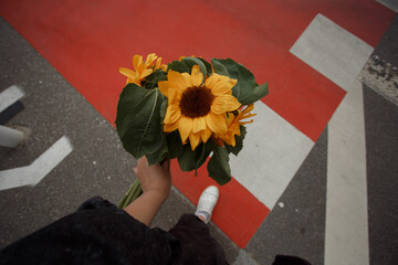 Young woman holds a bouquet of sunflowers in her hand on the  bright red pedestrian crossing background.