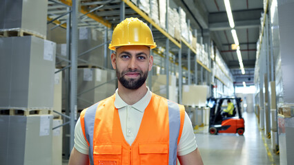 A man in a yellow hard hat and orange safety vest stands confidently in a warehouse, symbolizing...
