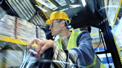 A man in a yellow hard hat and safety vest operates a forklift in a fast-paced warehouse,...
