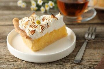 Piece of delicious pie with browned meringue and fork on wooden table, closeup