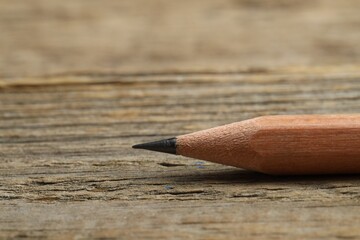 One sharp graphite pencil on wooden table, closeup. Space for text