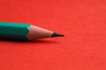 One sharp graphite pencil on red background, closeup. Space for text