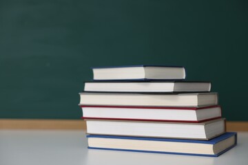 Stack of books on desk against chalkboard. Space for text