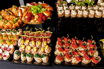 Assorted gourmet canapes and finger food on black trays at catered buffet table
