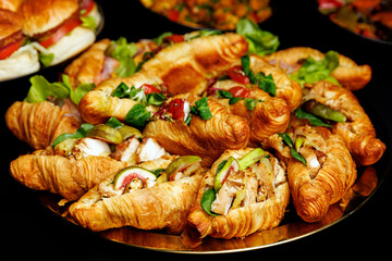 A tray of croissants with various toppings including lettuce and tomatoes. There are also sandwiches on the tray