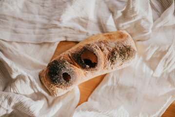 A burnt piece of bread with holes in it sits on a white cloth