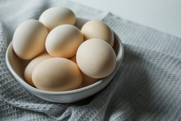 Fresh farm chicken eggs in bowl on grey kitchen towel close up