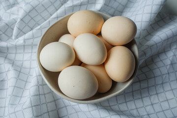 Fresh farm chicken eggs in bowl on kitchen towel close up