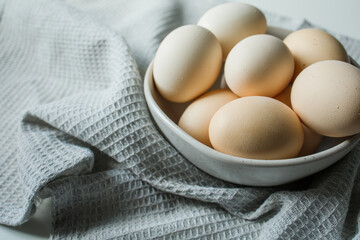 Fresh farm chicken eggs in bowl on grey kitchen towel close up