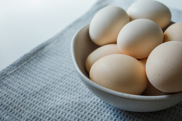 Fresh farm chicken eggs in bowl on grey kitchen towel close up