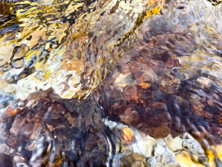 abstract water surface over rocky shore with strong color flow and light distortion. golden, amber and earthy tones. fluid visual