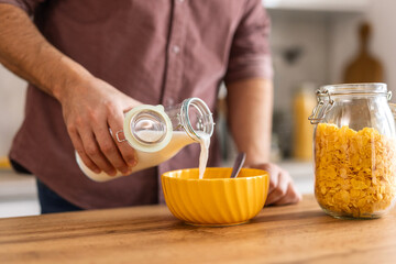 Man is preparing cereal for breakfast, pouring milk over a bowl of cereal in a cozy kitchen. everyday morning routine, evoking feelings of comfort, nourishment, and simplicity in the start of the day