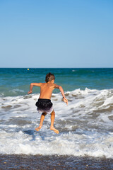 Boy jumping over waves on beach summer vacation fun