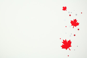 Canada Day flat lay concept. Scattered red paper maple leaves and star confetti on a white background. Minimalist festive design with copy space.