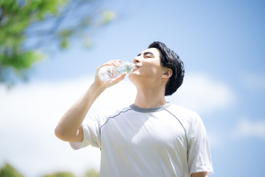  Close-up of a young man hydrating (drinking water) during the sport and exercise of running under a blue sky