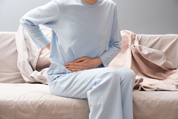 Girl in pajamas holding her stomach. Menstruation. Abdominal pain, hands of a woman with abdominal...