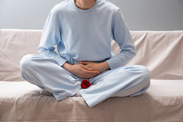 Obraz premium A girl in blue pajamas holds her stomach. There is a red rose next to her as a symbol of menstruation. Depression