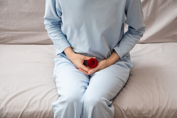 A girl in blue pajamas holds her stomach. There is a red rose next to her as a symbol of...