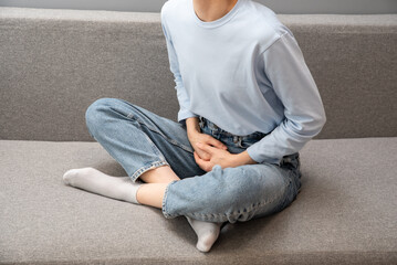 Girl in pajamas holding her stomach. Menstruation. Abdominal pain, hands of a woman with abdominal...