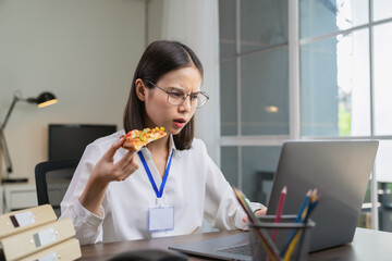 Asian businesswoman eating pizza while working with clients due to rush hour.