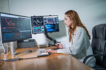 Finance professional analyzes market trends at dual monitor workstation in modern office setting