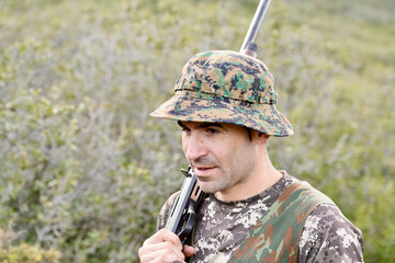 A man in camouflage hat and shirt holding a gun