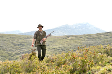 A man is walking through a field with a shotgun