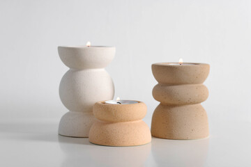 Stylish candlesticks with burning candles on white table