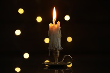 Burning candle in candlestick on mirror surface in darkness, bokeh effect
