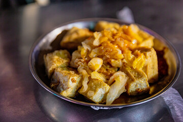 Angled view of a serving of Taiwanese stinky tofu garnished with pickled cabbage and spicy sauce, placed on a shiny metal table