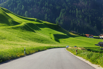 Scenic view small car drive countryside farm road green lush grass meadow mountain road alpine Austria on sunrise morning. Panoramic Alps grassland forest pasture path. Family car nature journey trip