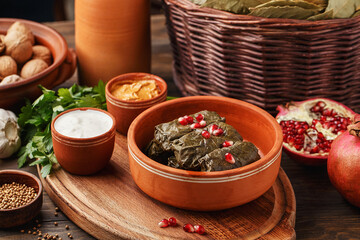 Traditional middle eastern dish dolma. Grape leaves stuffed with rice and meat. Tolma or sarma served in clay bowl with pomegranate seeds and various sauces. Side view
