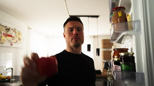 Creative point-of-view shot from inside a fridge as a man opens it, searches for ingredients, and grabs food. Bright kitchen lighting floods in, suggesting a home cooking or meal prep moment.