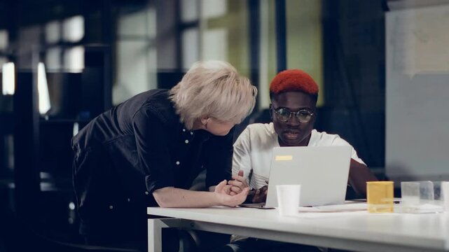 Business woman talking to African American colleague looking at laptop. Brainstorming constructive conversation.