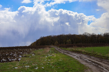 Rural landscape in Ukraine in early spring with a dirt road leading uphill through a field towards...