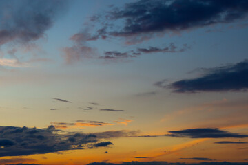 Captivating view of the evening sky during sunset. Dark blue and gray clouds contrast with the bright orange and pink hues of the sun setting below the horizon.