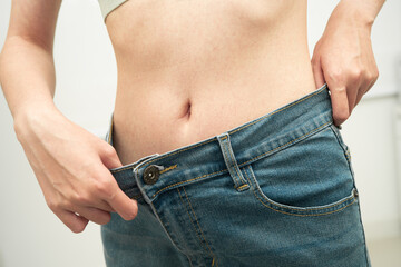 Fototapeta premium Young Asian woman losing weight wearing loose pants in oversize jeans.