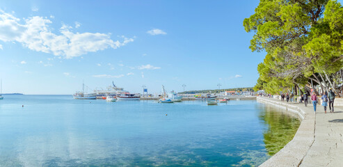 Fototapeta premium Barbariga, Peroj, Istria, Croatia: Boats in harbor, people stroll along the waterfront promenade