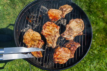 Grilled Pork Chops Cooking on Charcoal BBQ. Juicy pork chops sizzling on a charcoal grill with visible flames and smoke, perfect for an outdoor summer barbecue.