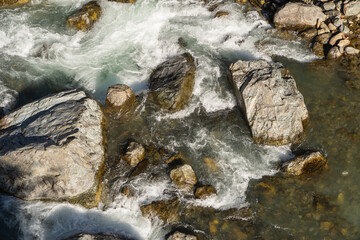 Mountain river flows in turbulent foaming stream in stone bed between huge boulders. Pure emerald...