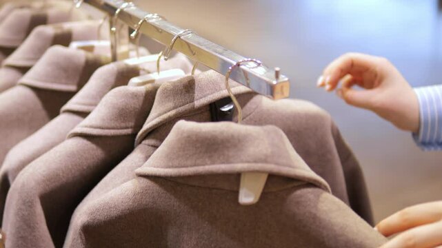 Person is looking at a rack of clothes. The clothes are hanging on a metal rack. The person is looking at the clothes and deciding which one to buy
