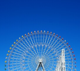 Colorful Ferris wheel against a deep blue sky in Osaka, Japan, showcasing modern architecture, vibrant symmetry, and urban entertainment.