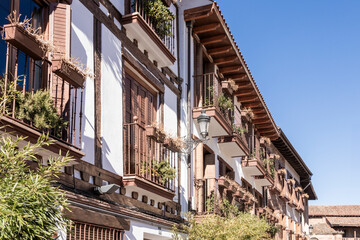A building with balconies and a balcony railing. The balconies are filled with plants. The building is white and brown